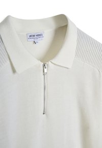 Maglione polo color crema chiaro con mezza zip frontale e dettagli a coste sul colletto e sulle spalle, realizzato in materiale morbido e testurizzato.