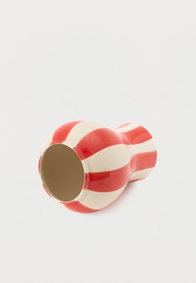 Κεραμικό βάζο με κόκκινες και λευκές ρίγες, ξαπλωμένο στο πλάι πάνω σε λευκό, απλό φόντο.