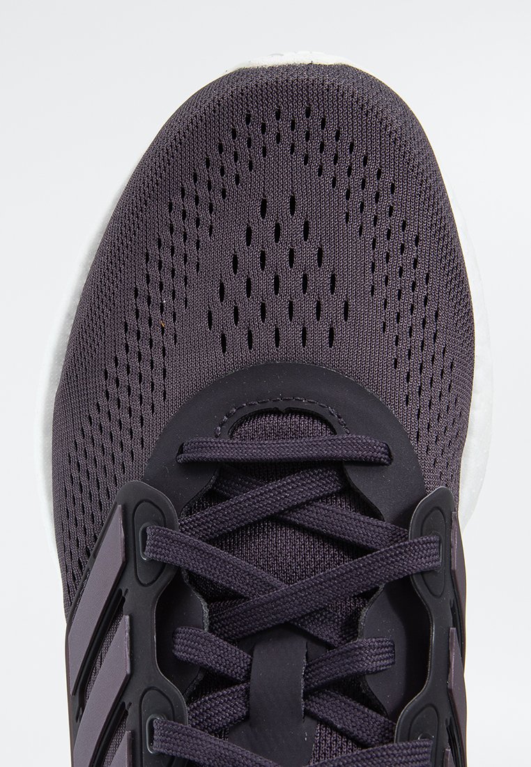 Chaussure de sport violette avec un dessus en mesh respirant, surface texturée et accents noirs. Présente un design à lacets et une semelle en caoutchouc.