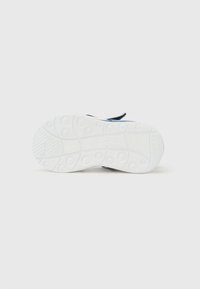 Πάτος παπουτσιού παιδικού μεγέθους, στραμμένος προς τα πάνω, με κυκλικά μοτίβα πέλματος και μια ορατή λουρίδα, σε απλό λευκό φόντο.