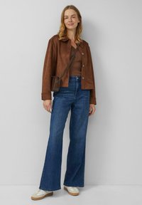 Brązowa zamszowa kurtka zapinana na guziki, w połączeniu z brązowym topem i wysokim stanem rozszerzanymi dżinsami. Dopełnieniem stroju są casualowe buty. Torebka z regulowanym paskiem.