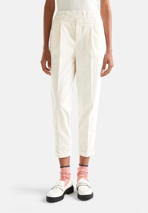 Pantalones de pana color crema con pliegues, ajuste relajado, dobladillos acampanados y bolsillos laterales, combinados con mocasines blancos y calcetines de volantes rosas.