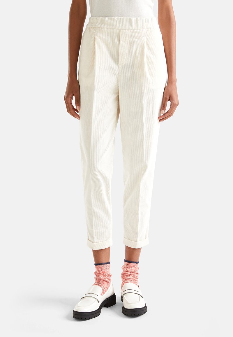 Crème-kleurige corduroy broek met plooien, comfortabele pasvorm, omgeslagen pijpen en zijzakken, gecombineerd met witte loafers en roze gecontrasteerde sokken.