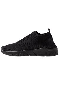 Crne pletene slip-on tenisice s teksturiranim gornjim dijelom, niskim dizajnom oko gležnja i izdržljivom gumiranom potplatom s uzorkom za pridržavanje.