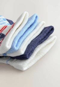 Seis pares de calcetines apilados. Los colores incluyen blanco, azul claro, azul marino y diseños estampados con acentos rojos. Textura suave.