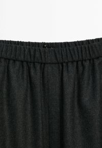 Ceinture grise texturée d'un pantalon avec un élastique froncé en haut. Le tissu semble doux, avec un motif subtil. Aucun élément métallique ou accent visible.