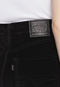 Czarne dżinsy z denimu o teksturowanej powierzchni, z skórzaną metką z napisem "Levi Strauss & Co." oraz krzywymi szwami na kieszeniach.