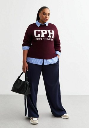 Suéter de punto burdeos con el texto "CPH COPENHAGUE", superpuesto a una camisa de rayas azul claro. Pantalones holgados azul marino con rayas blancas en los laterales. Bolso negro.