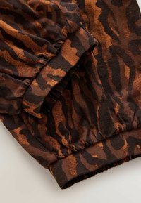 Hnedá a čierna látka so zvieracím vzorom s detailom nariasenej manžety, ktorá má mäkkú textúru a plynulý dizajn, ideálna na bežné nosenie.