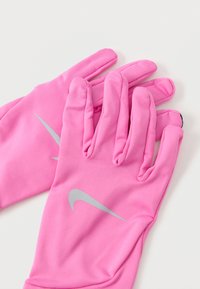 Par rokavici Nike v roza barvi z odsevnimi logotipi swoosh na hrbtni strani, razporejeni na beli podlagi.