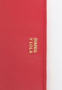 Cartera de cuero rojo con superficie texturizada, que presenta el logotipo dorado en relieve "BIMBA Y LOLA" exhibido de manera prominente.