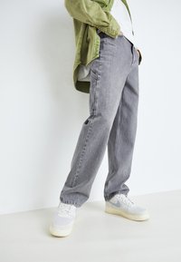 Pantalones de mezclilla gris con un corte relajado, que cuentan con cinco bolsillos. Combinados con zapatillas blancas y una chaqueta verde oliva.