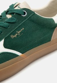 Zelené semišové tenisky s bielymi a tanskovými akcentmi, vybavené gumovou podrážkou a zlatým logom "Pepe Jeans" na boku.