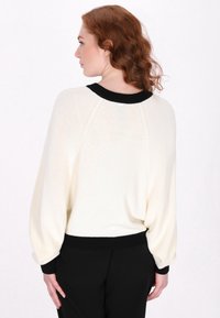 Maglione chiaro in crema con collo rotondo e polsini a coste neri; presenta spalle scese e un tessuto morbido e testurizzato.
