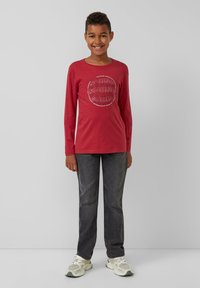 Rotes Langarm-T-Shirt mit kreisförmigem "SOUND"-Grafik, kombiniert mit dunkelgrauen Jeans und hellen Sneakers. Einfaches, lässiges Design.