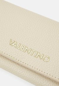 Beige textured leather wallet with embossed gold "VALENTINO" logo. Features stitched trim and smooth finish. Dimensions and closure not visible.