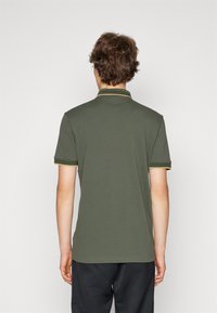 Pikétröja i olivgrön bomull med kontrasterande gula kragar och ärmsömmar, korta ärmar och rak fåll.