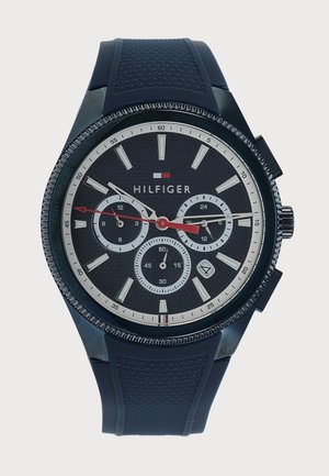 Schwarze Tommy Hilfiger Armbanduhr mit drei Unterzifferblättern, rotem Sekundenzeiger, weißen Stundenmarkierungen und strukturiertem schwarzem Kautschukarmband.