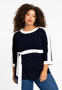 Dunkelblaues und weißes Langarmoberteil mit Rundhalsausschnitt, einem gebundenen Taillengürtel und kontrastierenden weißen Streifen an den Ärmeln. Glatte Stofftextur.