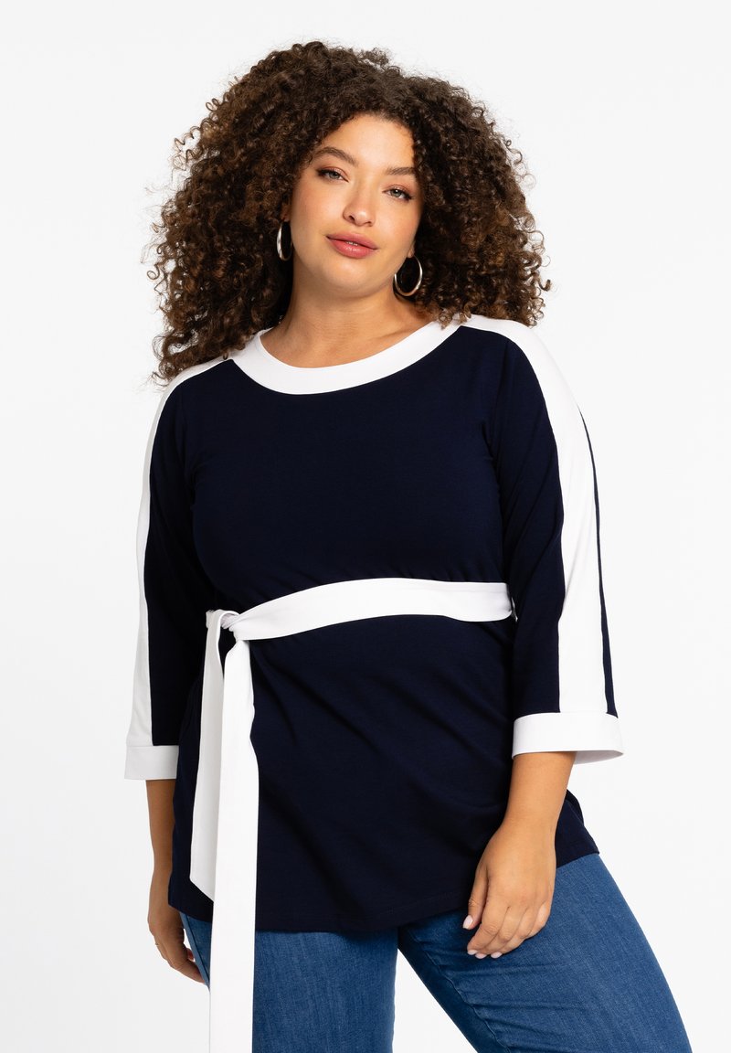 Dunkelblaues und weißes Langarmoberteil mit Rundhalsausschnitt, einem gebundenen Taillengürtel und kontrastierenden weißen Streifen an den Ärmeln. Glatte Stofftextur.