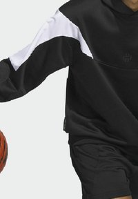 Personne portant une tenue de sport noire et blanche à manches longues dribblant un ballon de basket orange sur un fond uni.