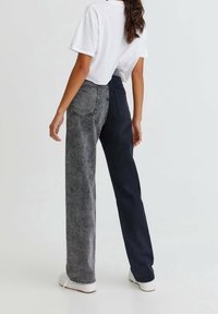 Vaqueros de pierna ancha con un diseño dividido: un lado en denim oscuro y el otro en gris claro. Presenta dos bolsillos traseros y una cintura alta.