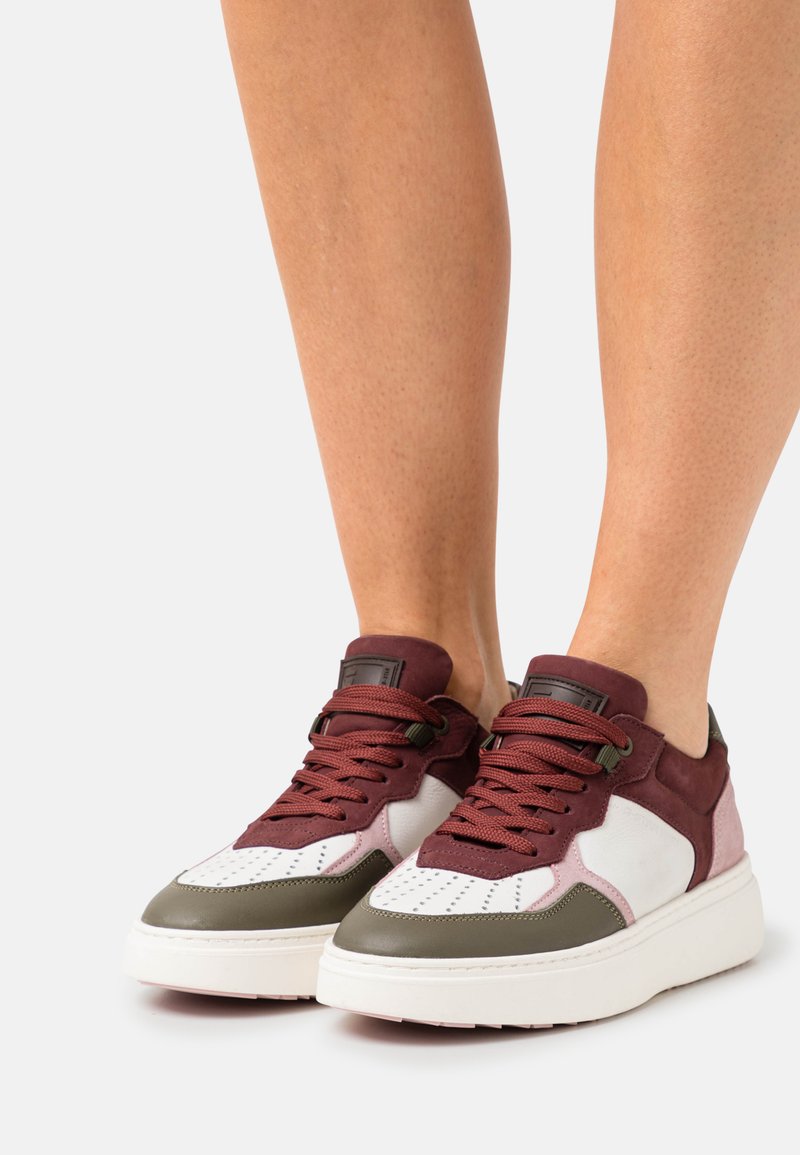 Sneakers met een witte leren neus, bovenwerk van bordeauxrode suede en olijfgroene accenten; dikke witte zool; ronde veters; geperforeerde details.