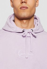 Felpa lavanda con cappuccio dotata di coulisse nera, tasca a marsupio frontale e logo ricamato bianco sul petto.