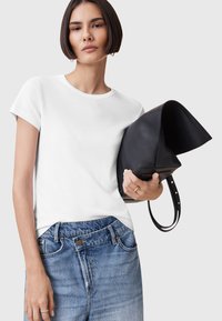 T-shirt bianco aderente a maniche corte, abbinato a jeans blu a vita alta. La modella tiene una borsa nera in pelle con un design strutturato.