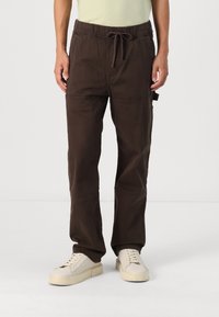 Brown elasticated cargo pants with pockets, a drawstring waist, and a relaxed fit, paired with off-white sneakers.