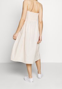 Jasno beżowa sukienka z marszczoną górą i cienkimi ramiączkami, płynący dół sięgający do połowy łydki. Noszona z białymi trampkami. Gładka tekstura.