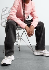 Rosa sweatshirt med rund hals, tillsammans med mörkgrå kordflödspants och vita sneakers, sittande på en stålstol.