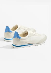 Weiße Sneakers mit blauen Akzenten, verfügen über ein glattes Obermaterial, Schnürdesign und eine strukturierte Wildleder-Fersenstütze mit einem kontrastierenden blauen Streifen.