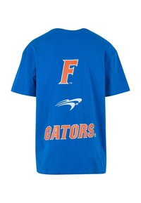Sinine puuvillane T-särk, mille esiküljel on oranžid "F" ja "GATORS" ning nende vahel valge logo. Lühikesed varrukad ja tavaline ümmargune kaelus.