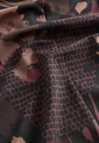 Tissu avec un motif abstrait multicolore dans des tons de noir, bordeaux et taupe, présentant une texture lisse et un léger éclat.