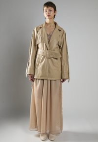 Beige Lederjacke mit Fransen, tailliert mit einem Gürtel, kombiniert mit einem beige fließenden Maxikleid und off-white Stiefeletten.