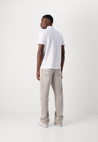 Hvid polo shirt med krave-design, parret med lysegrå, afslappede bukser og hvide sneakers med røde accenter.