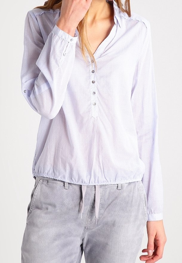 Chemise bleu clair à boutons avec col, manches longues, ourlet élastique et petits pois blancs subtils. Associée à un pantalon gris clair.