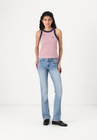 Débardeur rayé rouge et blanc avec bordure bleu marine ; associé à un jean évasé bleu clair ; chaussures noires ; le modèle se tient devant un fond uni.