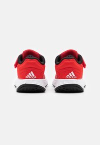 Baskets de sport rouge et noire au design léger, présentant une tige texturée, un col rembourré et un logo distinctif à trois bandes.