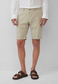 Hellebeige Shorts aus strukturiertem Stoff, mit Knopfverschluss, seitlichen Taschen und umgeschlagenen Säumen, kombiniert mit braunen flachen Sandalen.