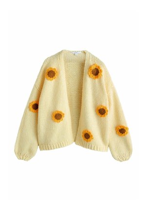 Gelber gestrickter Cardigan mit übergroßen Ärmeln, der vorne mit bestickten Sonnenblumen in verschiedenen Größen verziert ist. Vorderseite offen gestaltet.