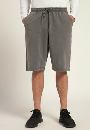 Grijze shorts van zachte stof, met een elastische tailleband met trekkoord, zijzakken en een knielange snit. Draagt zwarte sneakers.