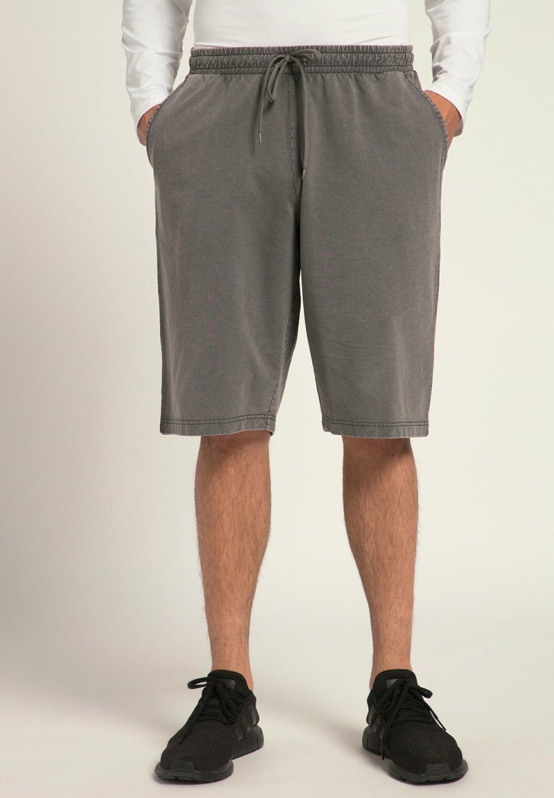 Shorts gris en tissu doux, dotés d'une taille élastique avec cordon de serrage, de poches latérales et d'une coupe mi-genou. Portés avec des baskets noires.