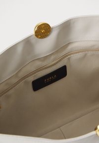 Innenansicht einer weißen Leder-Shopper-Tasche mit goldenen Beschlägen, beigem Futter, einem Reißverschlussfach und einem schwarzen Etikett mit goldener Schrift.