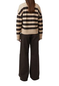Beżowo-brązowy sweter w paski o prążkowanej fakturze i krótkim kroju. Połączony z ciemnobrązowymi, szerokimi spodniami.