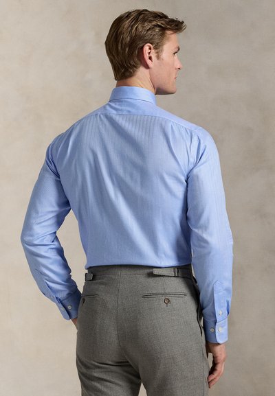 Cămașă albastru deschis, cu mâneci lungi și un model subtil cu dungi. Pantaloni gri cu două buzunare la spate și detalii cu nasturi. Croială cambrată.