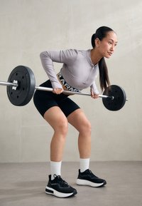 Sorte vektskiver ligger på en sølvfarget vektstang. En person i en lys grå zip-up genser og svarte shorts utfører en bent-over row. Sorte sneakers og hvite sokker.