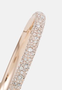 Ring aus Roségold mit einem glatten Band, das mit mehreren klaren Kristallen in unterschiedlichen Größen besetzt ist und eine strukturierte, schimmernde Oberfläche schafft.