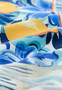 Gėlių raštų audinys mėlynais ir geltonais raštais, pasižymintis minkštu tekstūrų pojūčiu ir lygiu paviršiumi. Išskirtinės sukaustytos kraštinės ir ryškios spalvos.